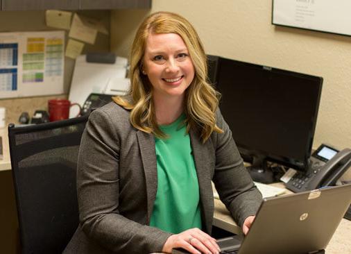 female business professional smiles while sitting at desk in front of computer